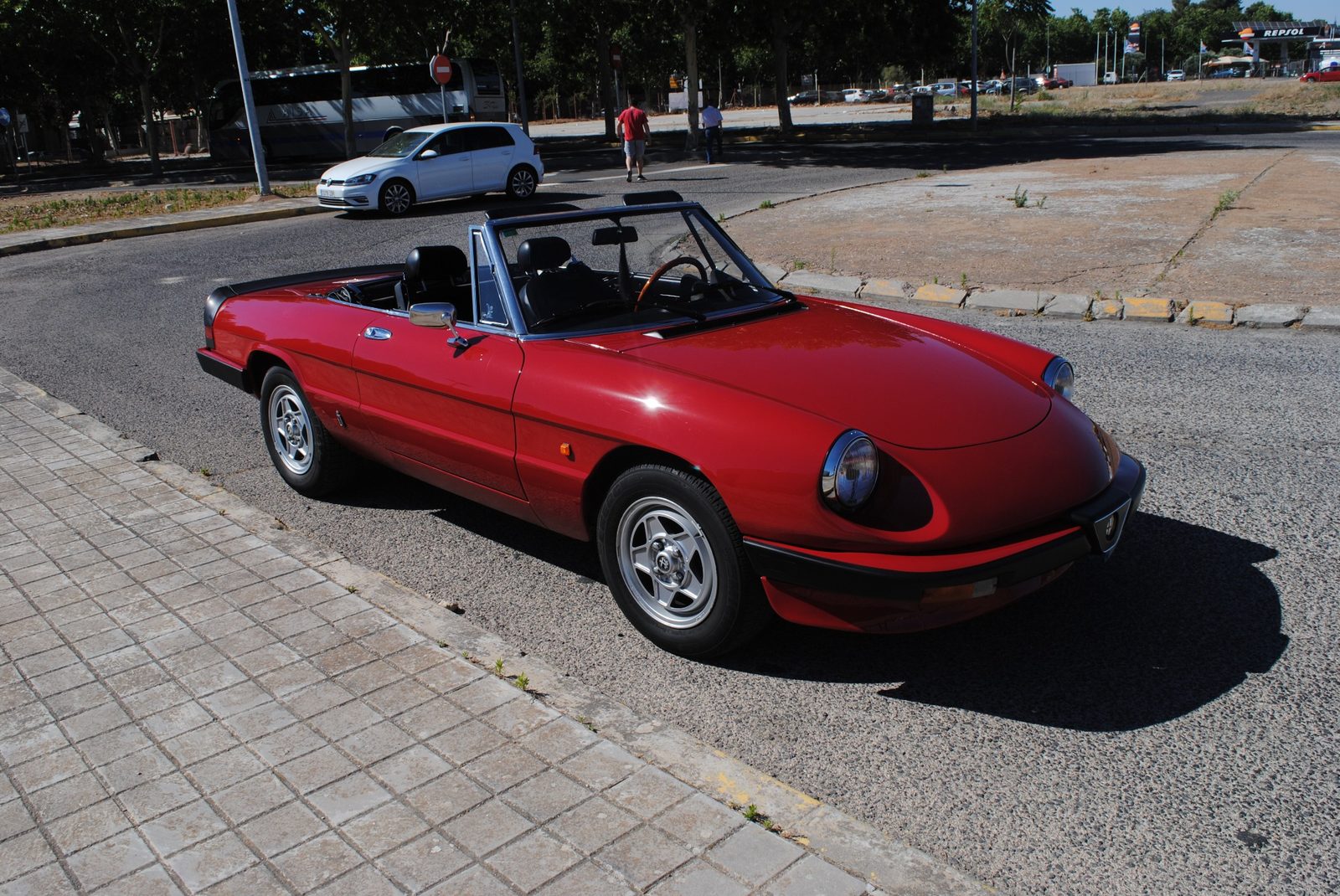 Alfa Romeo Spider 2.0 de 1985 de color rojo, descapotado, aparcado en el arcén de una calle bajo el sol.