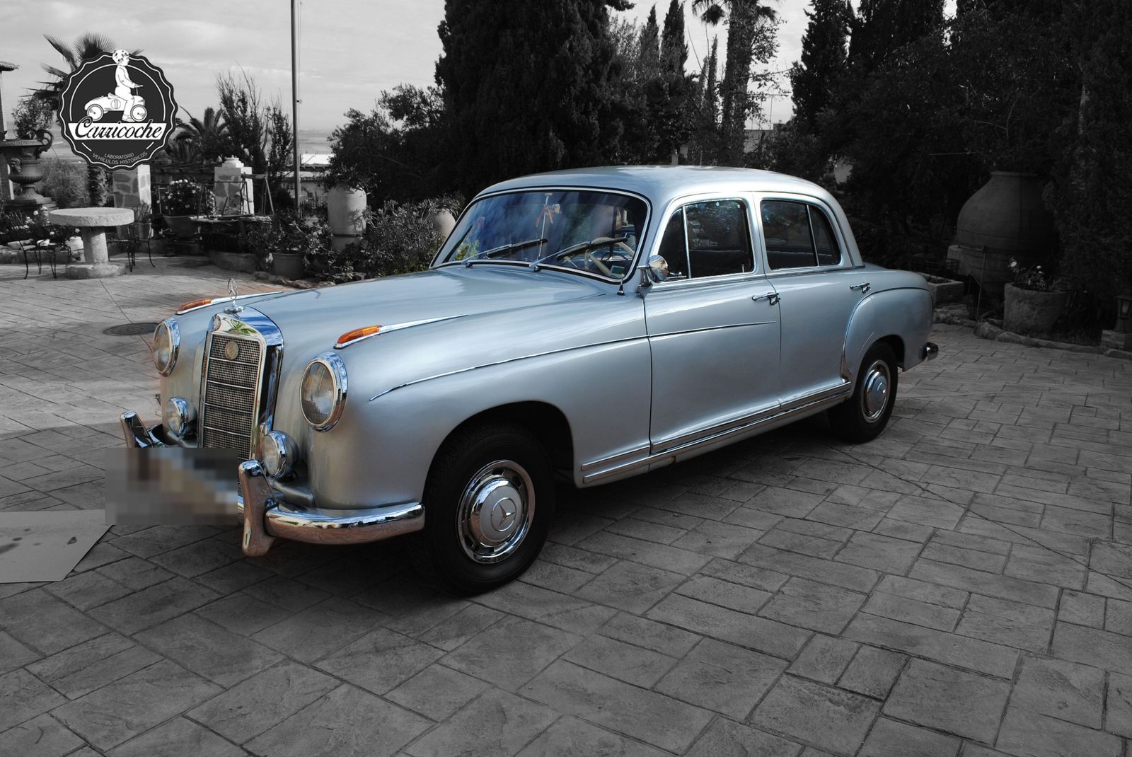 Mercedes-Benz 220 S (W180) de 1958 en color gris plata, aparcado en el patio de una finca.