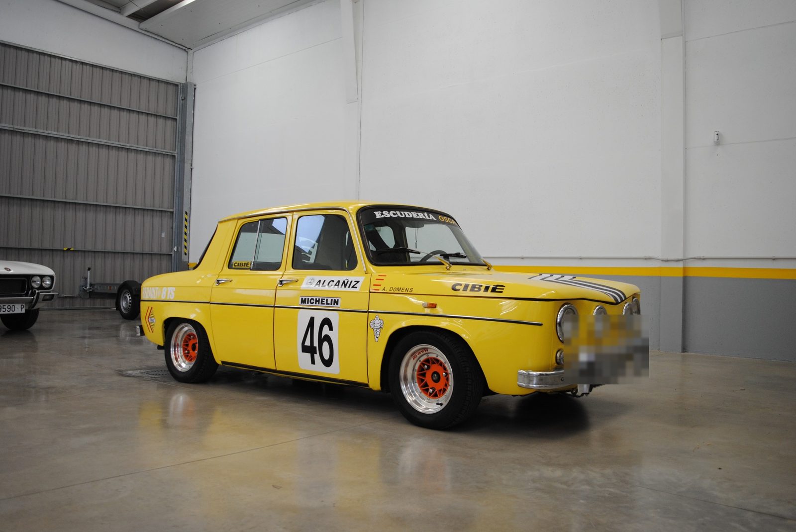 Renault 8 TS de 1968 con decoración amarilla de competición y el dorsal 46, aparcado en una nave junto a otra unidad del mismo modelo.